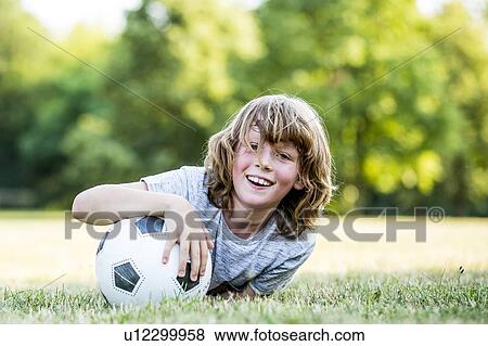 Boy holding football while lying in park, smiling, portrait. View Large Photo Image Stock Photo - Boy holding football while lying in park, smiling, portrait.. Fotosearch
