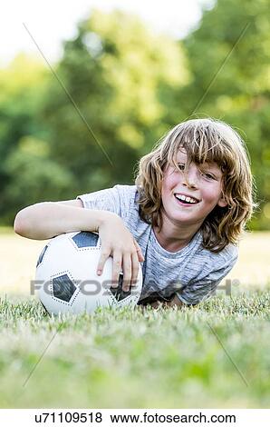 Stock Photo - Boy holding football while lying in park, smiling, portrait.. Fotosearch