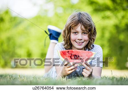 Picture - Boy holding watermelon while lying in park, smiling, portrait.. Fotosearch