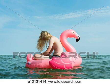 Picture - Boy on inflatable flamingo at sea. Fotosearch
