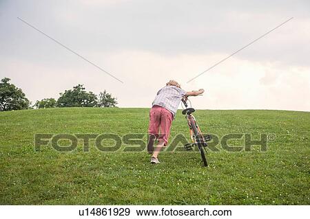 Stock Photo - Boy pushing bicycle uphill. Fotosearch