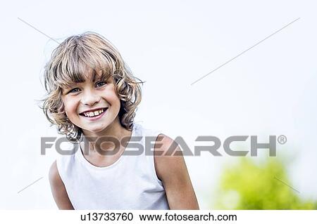 Stock Image - Boy with blonde hair smiling in park, portrait.. Fotosearch