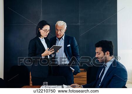 Stock Image - Businessman and woman looking at digital tablet in boardroom. Fotosearch