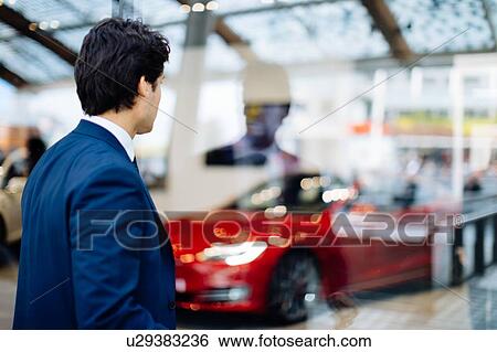 Businessman looking through glass wall at sports car in showroom View Large Photo Image Stock Photograph - Businessman looking through glass wall at sports car in showroom. Fotosearch