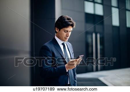 Stock Photo - Businessman using smartphone in front of office building. Fotosearch