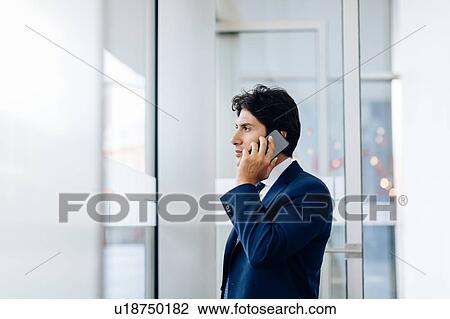 Stock Image - Businessman using smartphone in office building. Fotosearch