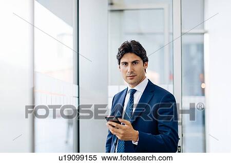Businessman using smartphone in office building View Large Photo Image Stock Photography - Businessman using smartphone in office building. Fotosearch