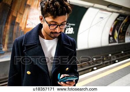 Stock Image - Businessman using smartphone on platform of subway station, London, UK. Fotosearch