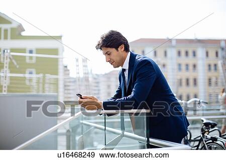 Businessman using smartphone on terrace View Large Photo Image Stock Photo - Businessman using smartphone on terrace. Fotosearch