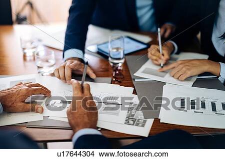 Businessmen and woman at boardroom table working on paperwork, cropped View Large Photo Image Picture - Businessmen and woman at boardroom table working on paperwork, cropped. Fotosearch
