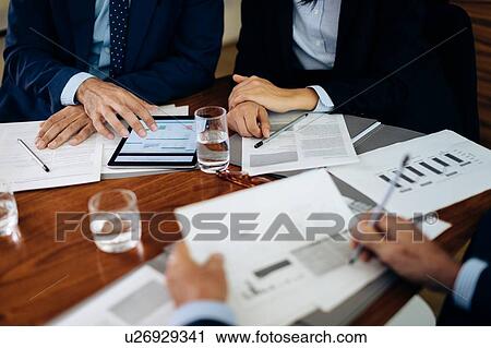 Businessmen and woman at boardroom table using digital tablet and working on paperwork, cropped View Large Photo Image Stock Image - Businessmen and woman at boardroom table using digital tablet and working on paperwork, cropped. Fotosearch