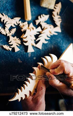 Stock Image - Carpenter chiseling edge of wooden christmas tree at workbench, close up of hands. Fotosearch