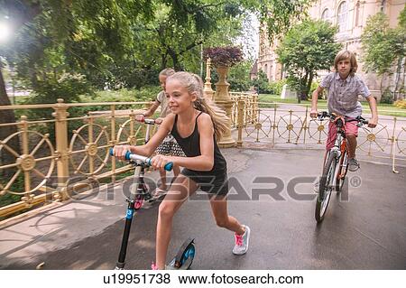 Stock Photo - Children cycling and riding on scooter in park. Fotosearch