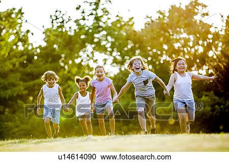 Stock Image - Children holding hands and running in park, laughing.. Fotosearch