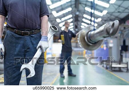 Stock Photography - Close up of engineer holding large spanner in gearbox factory. Fotosearch