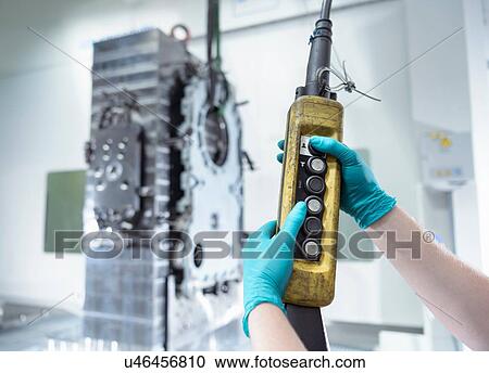 Stock Image - Close up of engineer using crane to lift parts onto CNC machine. Fotosearch