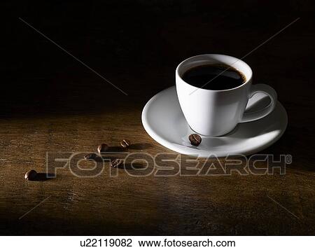 Stock Image - Coffee in coffee cup with beans on wooden table.. Fotosearch