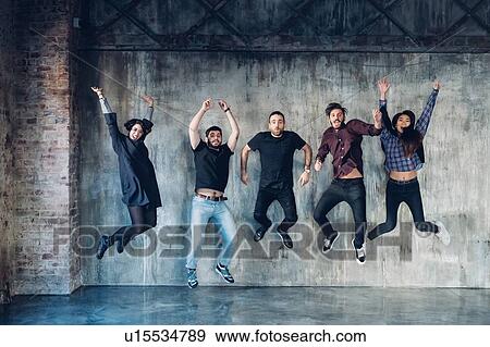 Stock Photo - Colleagues in jumping pose for group photo against concrete wall. Fotosearch