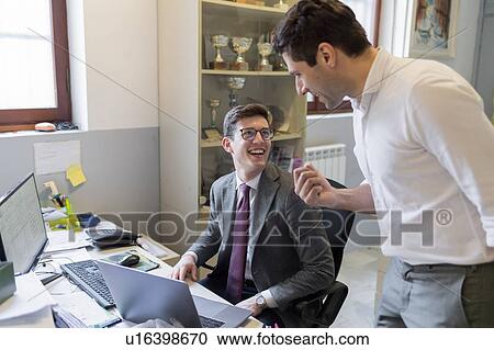 Stock Image - Colleagues laughing in office. Fotosearch