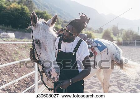 Stock Photo - Cool young man bonding with horse in rural equestrian arena. Fotosearch