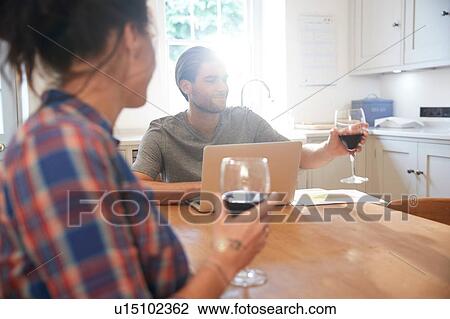 Couple at kitchen table drinking red wine while using laptop View Large Photo Image Stock Image - Couple at kitchen table drinking red wine while using laptop. Fotosearch