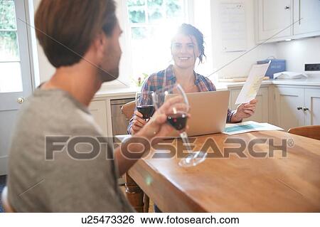 Stock Photograph - Couple at kitchen table drinking red wine while doing paperwork. Fotosearch