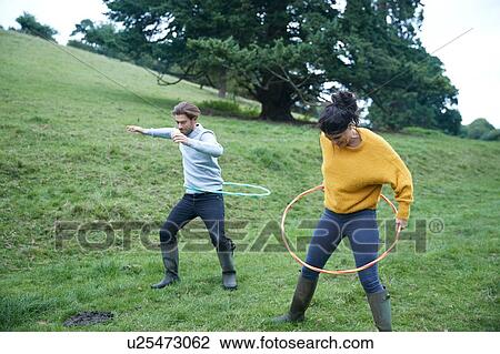 Stock Image - Couple hula hooping in field. Fotosearch
