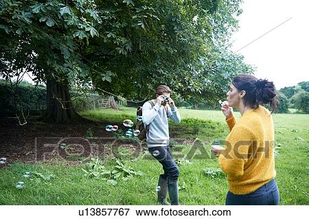 Stock Photo - Couple playing with soap bubbles in field. Fotosearch
