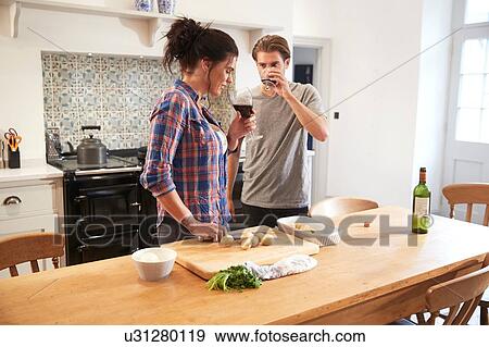 Stock Photo - Couple preparing food and drinking wine at kitchen table. Fotosearch