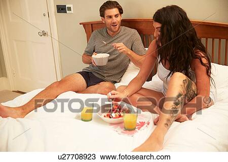 Stock Image - Couple sharing fruit and orange juice breakfast in bed. Fotosearch