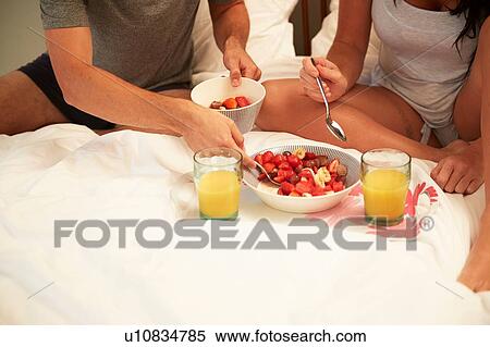 Stock Photography - Couple sharing fruit and orange juice breakfast in bed, cropped. Fotosearch
