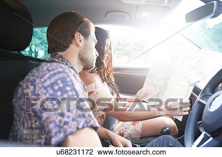 Stock Image - Couple sitting in car looking at folding map. Fotosearch