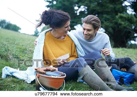 Picture - Couple sitting in rural field cooking on barbecue grill. Fotosearch