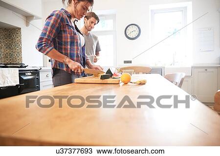 Stock Image - Couple slicing fresh fruit at kitchen table. Fotosearch