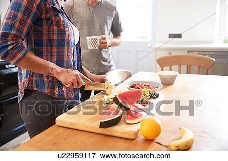Couple slicing fresh fruit at kitchen table, mid section View Large Photo Image Stock Photo - Couple slicing fresh fruit at kitchen table, mid section. Fotosearch