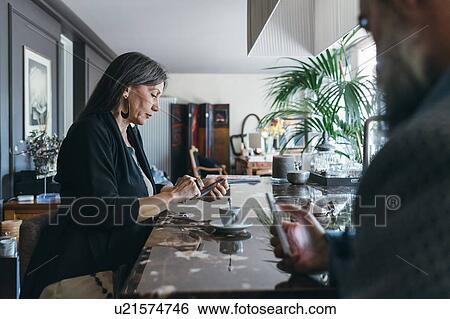 Stock Photograph - Couple using cellphone over coffee in kitchen. Fotosearch
