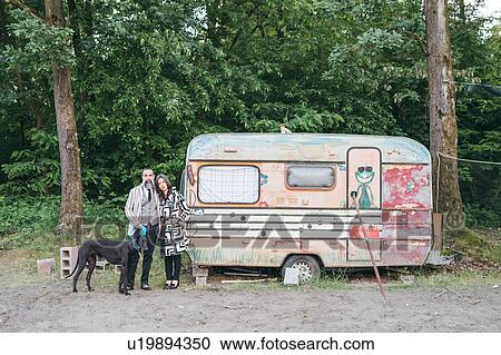 Stock Image - Couple walking dog standing by caravan. Fotosearch