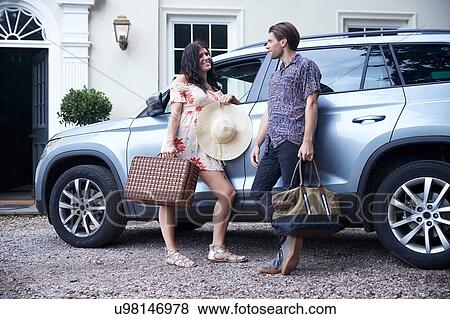 Stock Photo - Couple with suitcases leaning against car outside hotel front door. Fotosearch