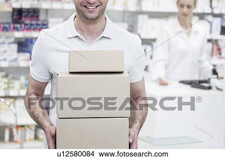 Picture - Courier carrying boxes in pharmacy with pharmacist in background.. Fotosearch