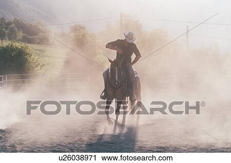 Stock Image - Cowboy horse riding in dusty equestrian arena, Primaluna, Trentino-Alto Adige, Italy. Fotosearch