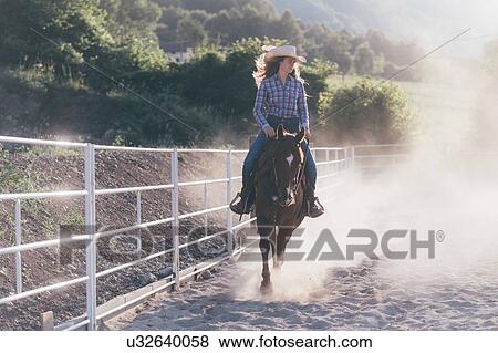 Stock Photo - Cowgirl horse riding in dusty equestrian arena, Primaluna, Trentino-Alto Adige, Italy. Fotosearch