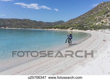 Stock Photo - Cyclist doing wheelie on beach, Villasimius, Sardinia, Italy. Fotosearch