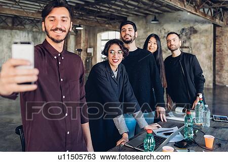 Stock Image - Designer and colleagues taking selfie at meeting table. Fotosearch