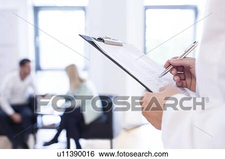 Doctor making notes in foreground with patients in background. View Large Photo Image Stock Photograph - Doctor making notes in foreground with patients in background.. Fotosearch