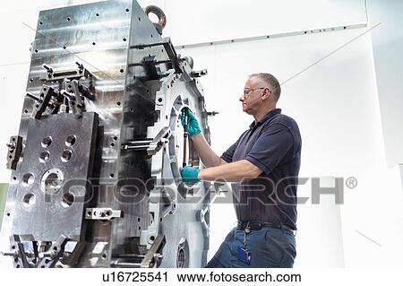 Stock Image - Engineer checking part on large CNC machine in gearbox factory. Fotosearch