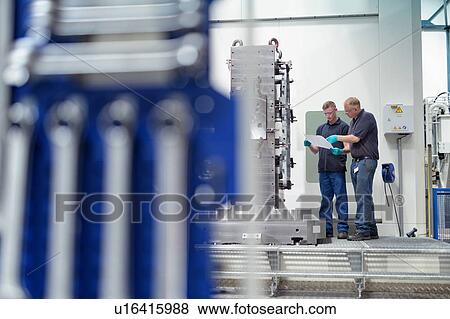 Stock Photo - Engineer instructing ap0entice on CNC machine in gearbox factory. Fotosearch