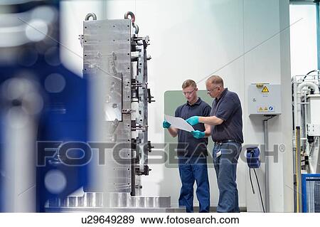 Stock Photo - Engineer instructing ap0entice on CNC machine in gearbox factory. Fotosearch