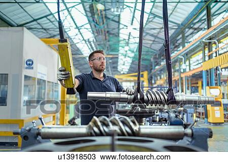 Stock Image - Engineer moving partly finished gear parts in gearbox factory. Fotosearch