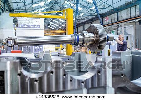 Stock Photo - Engineer using crane to position large gear with spindle in gearbox factory. Fotosearch