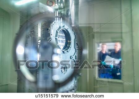 Stock Photo - Engineers viewing part inside CNC machine in gearbox factory. Fotosearch